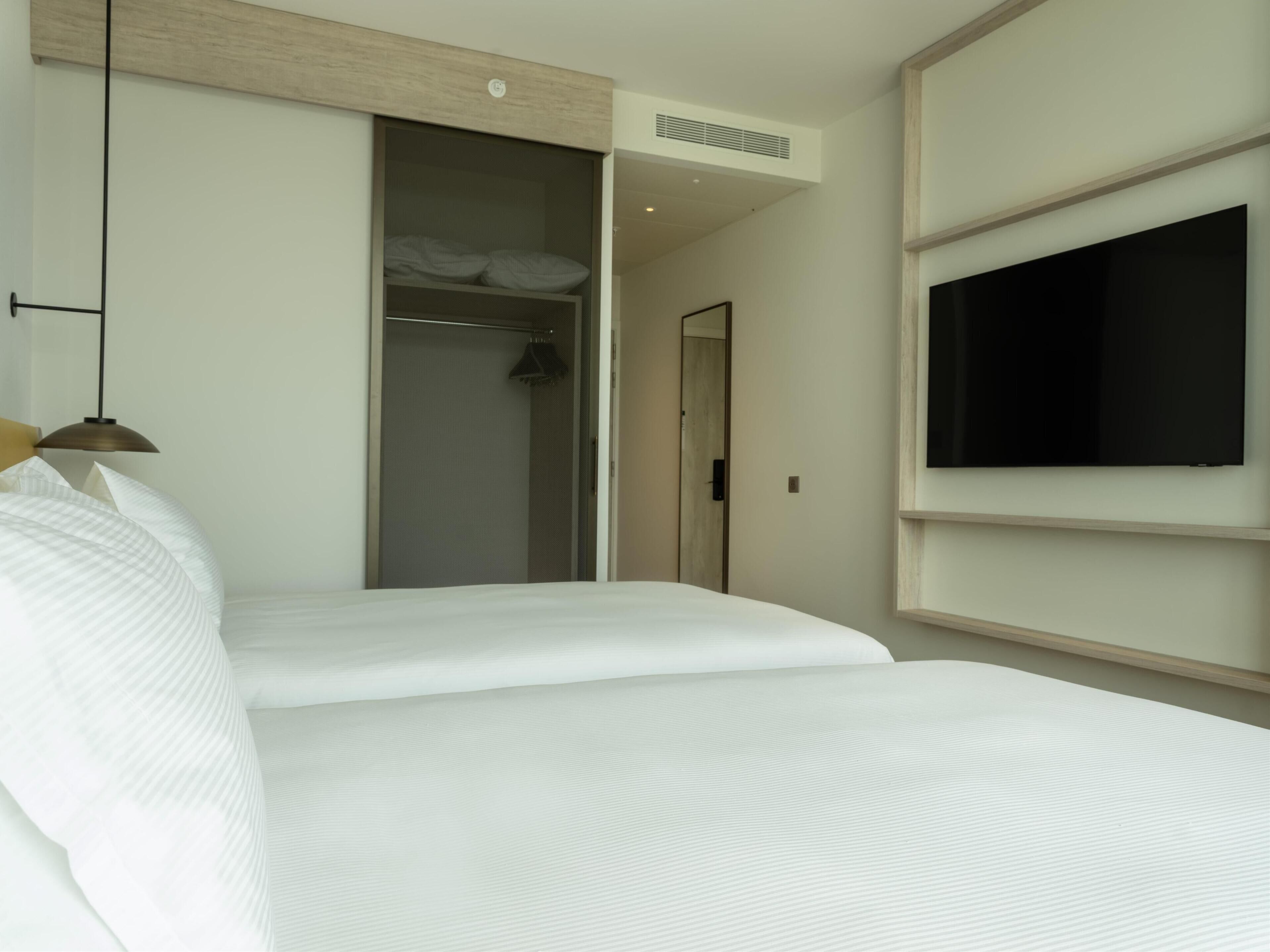 Une chambre d’hôtel équipée d’un lit, d’une armoire, d’un téléviseur et d’un luminaire suspendu.