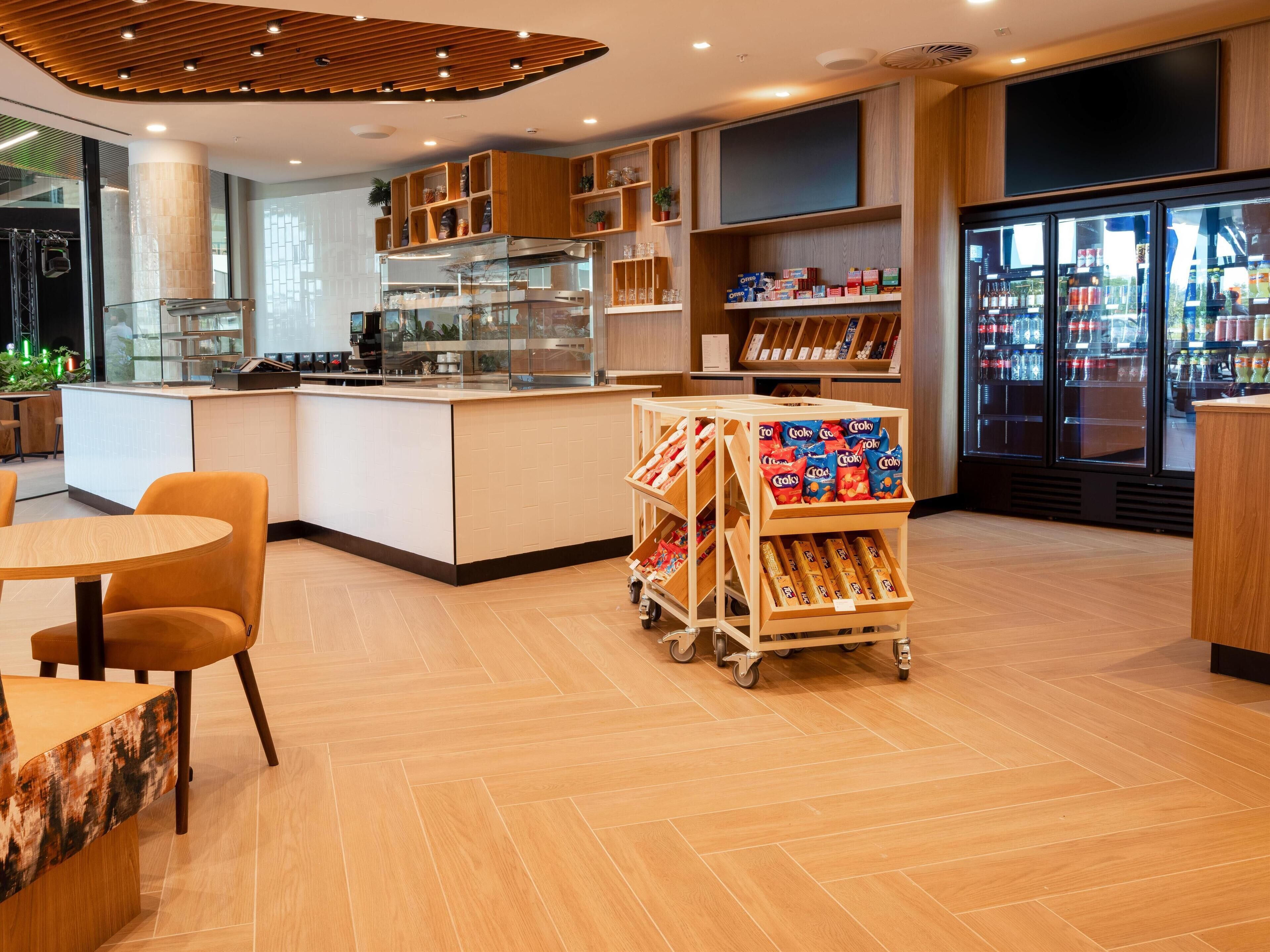 A modern cafe with a wooden counter, seating area, and a refrigerated display case.