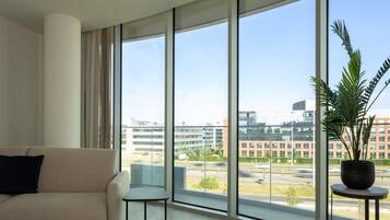 A modern living room with a beige sofa, a small side table, and a large window offering a view of a cityscape.