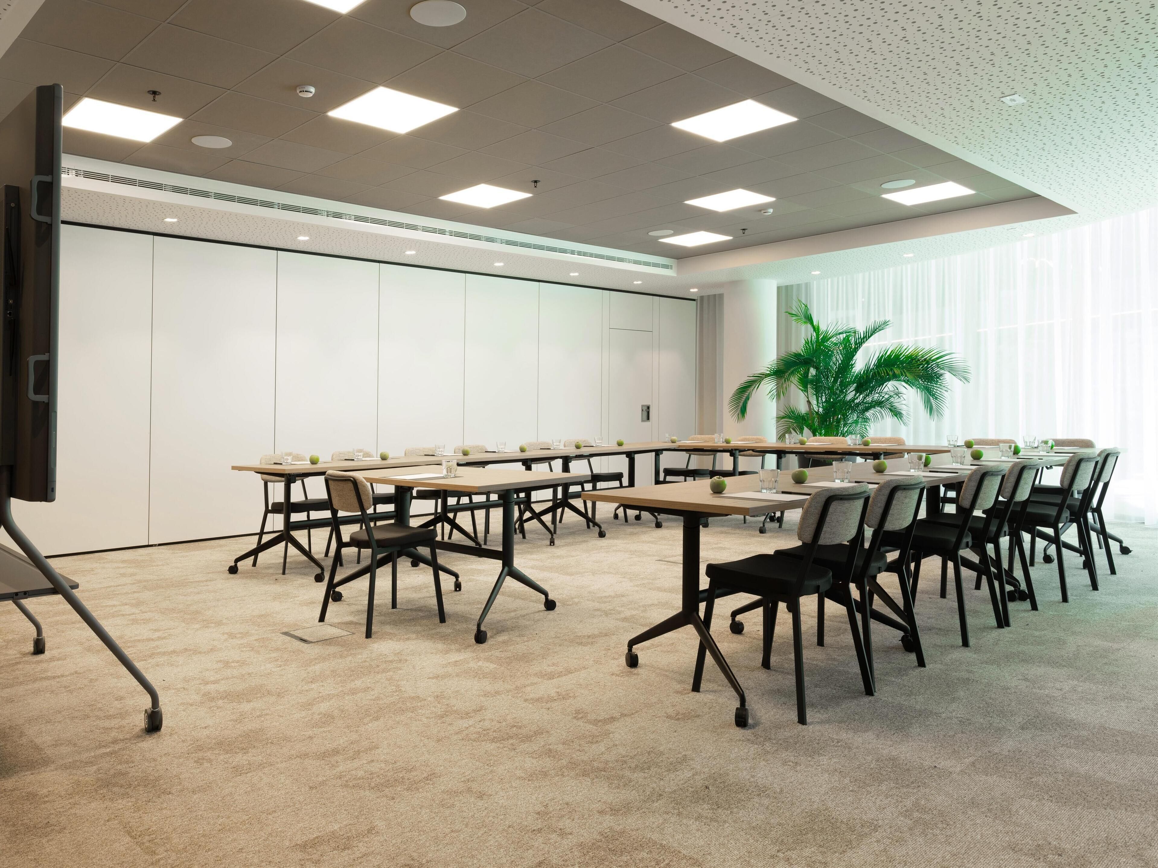 A conference room with a long table, chairs, a projector screen, and a large window with blinds.