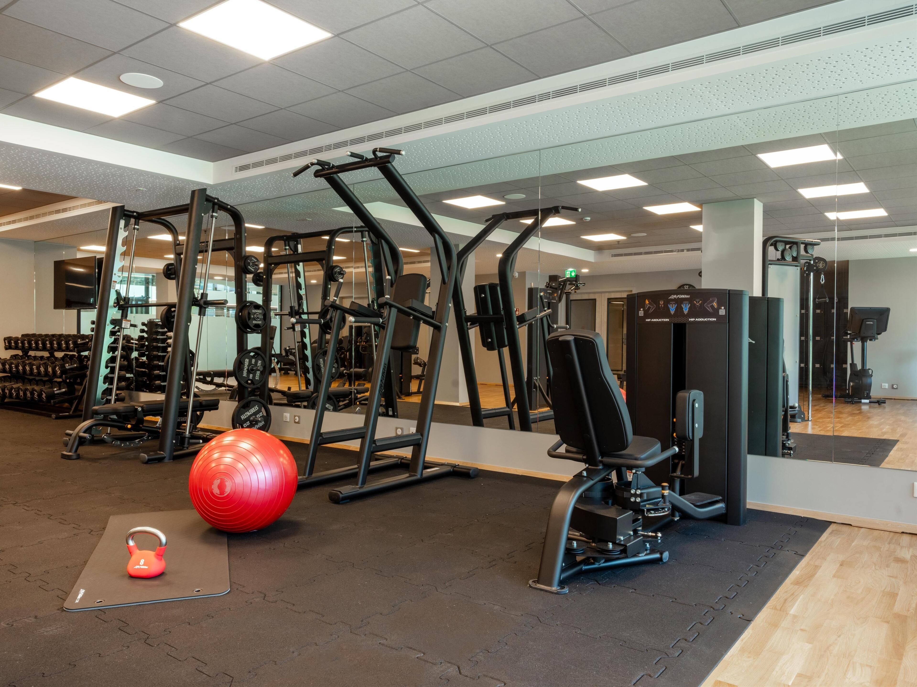 A gym with exercise equipment, a red exercise ball, and a kettlebell on a mat.