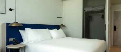 A hotel room with a bed, bedside table, lamp, and a shower area.