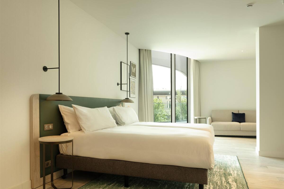Ein modernes Hotelzimmer mit einem großen Bett, einem Nachttisch, einem kleinen Tisch, einer Couch und einem großen Fenster mit Blick.