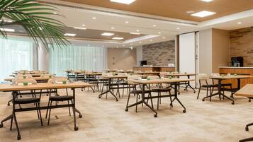 A conference room with multiple tables, chairs, and a kitchen area.