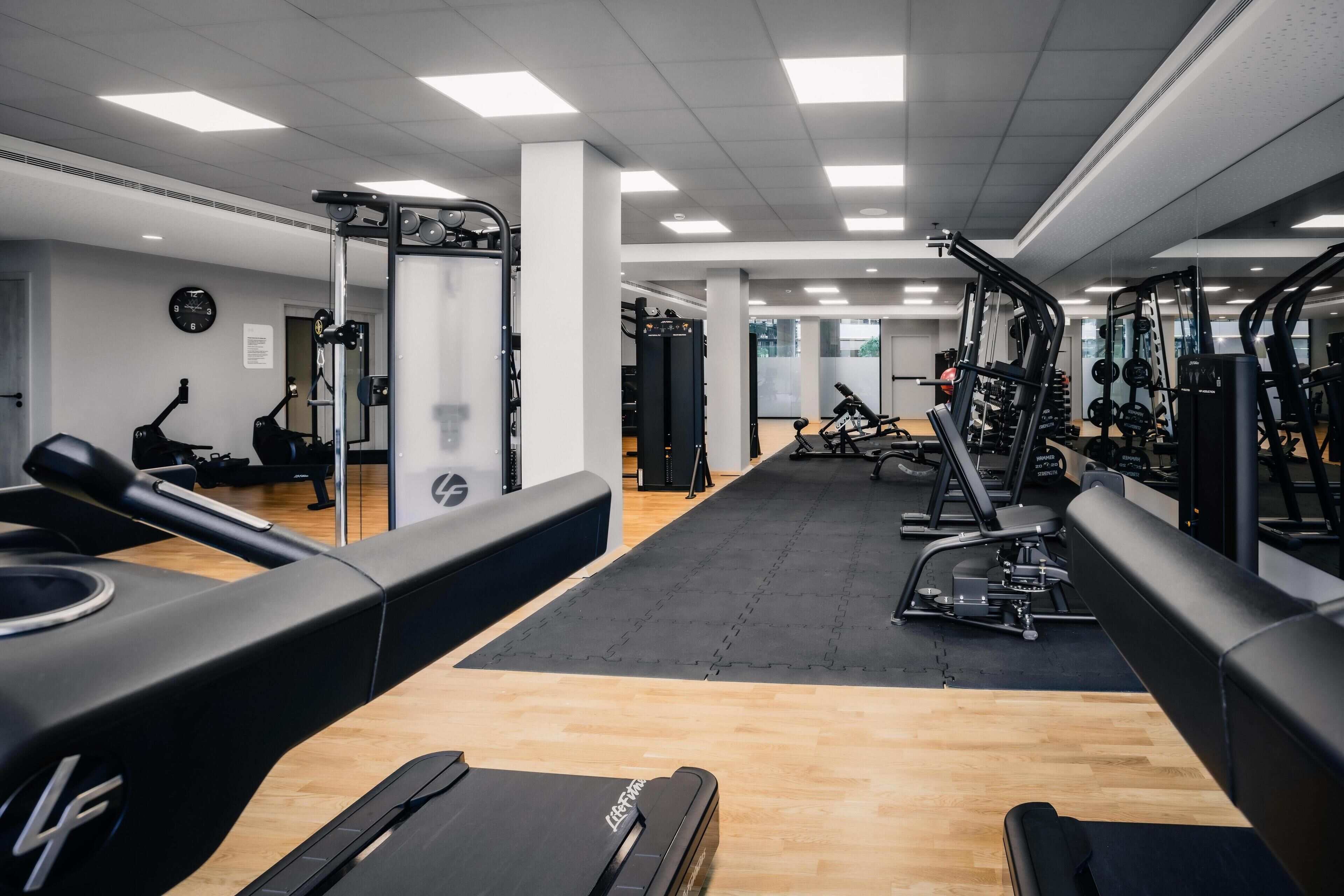 Un gimnasio con máquinas de cardio, equipo de levantamiento de pesas y un espejo grande.