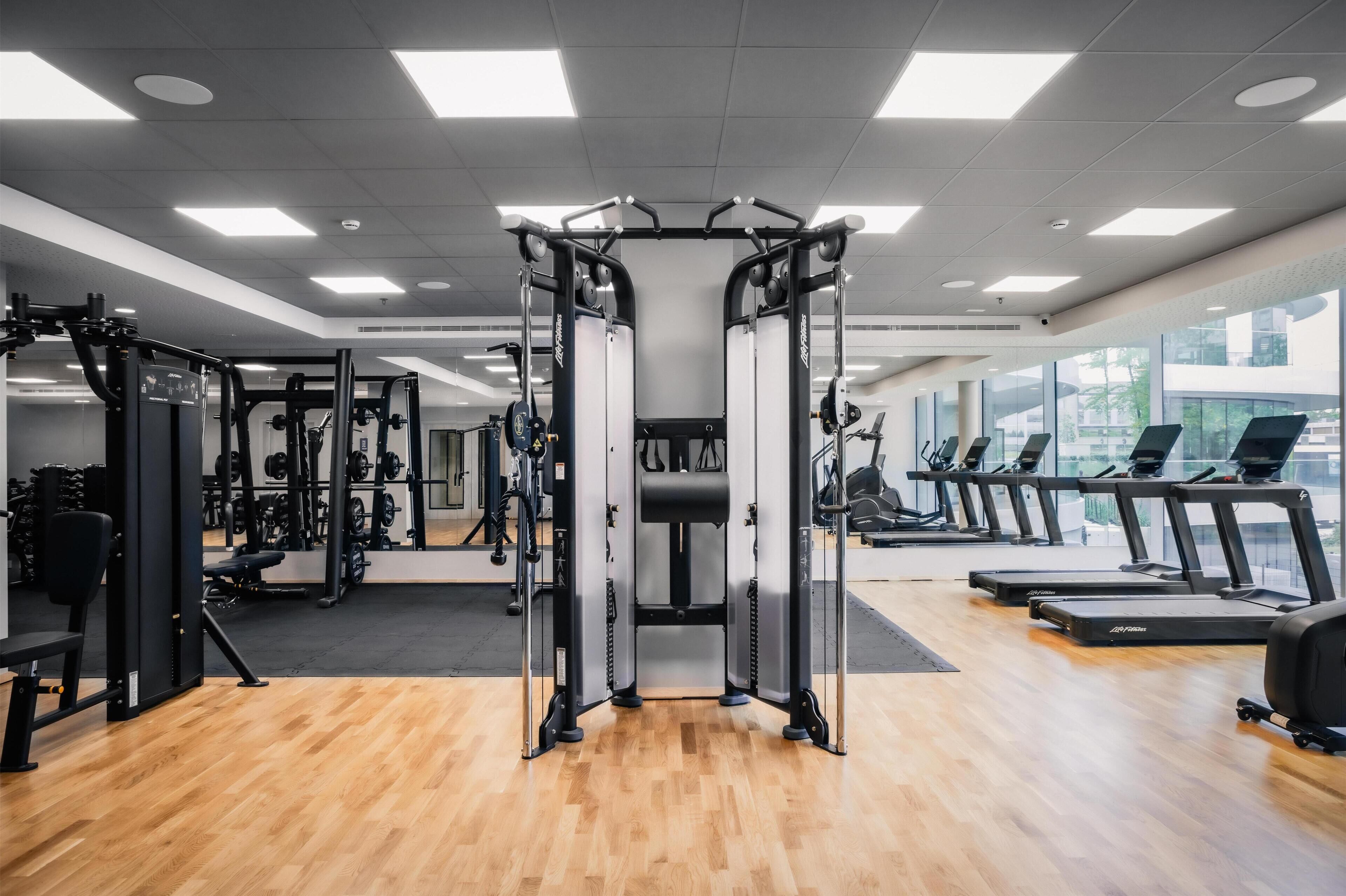 Un gimnasio con máquinas de pesas, cintas de correr y un espejo grande.