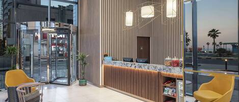 A modern reception area with a glass entrance, wooden paneling, and a counter with a computer and a small shelf.
