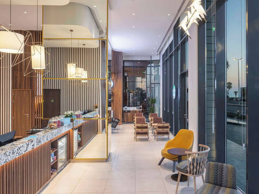 Un moderno vestíbulo de hotel con un mostrador de recepción, una zona de estar y grandes ventanales con vistas a la ciudad.