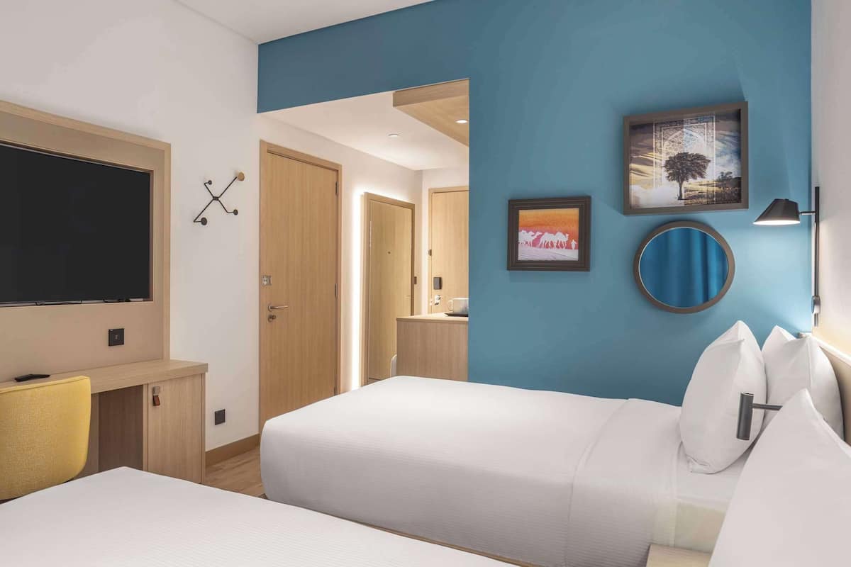 A hotel room with a bed, a desk, a chair, a TV, and a bathroom visible through an open door.