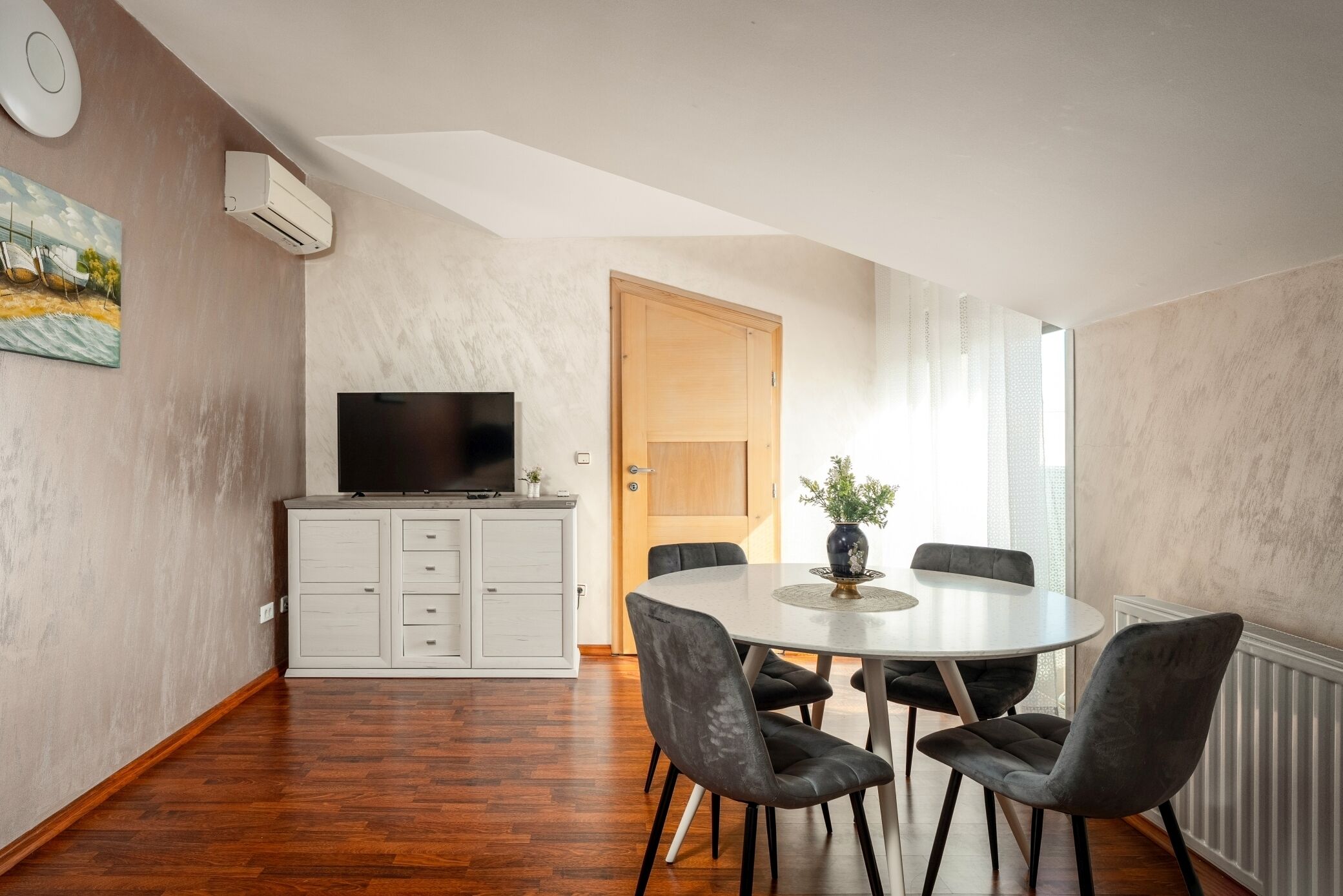 Ein Essbereich mit einem runden Tisch, vier Stühlen, einem Fernseher auf einem Schrank und einer Tür zu einem anderen Raum.