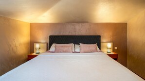 Quarto de hotel com uma cama grande, duas mesas de cabeceira com luminárias e uma cabeceira escura.