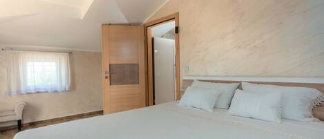 A bedroom with a large bed, a wooden wardrobe, a chair, and a window with curtains.