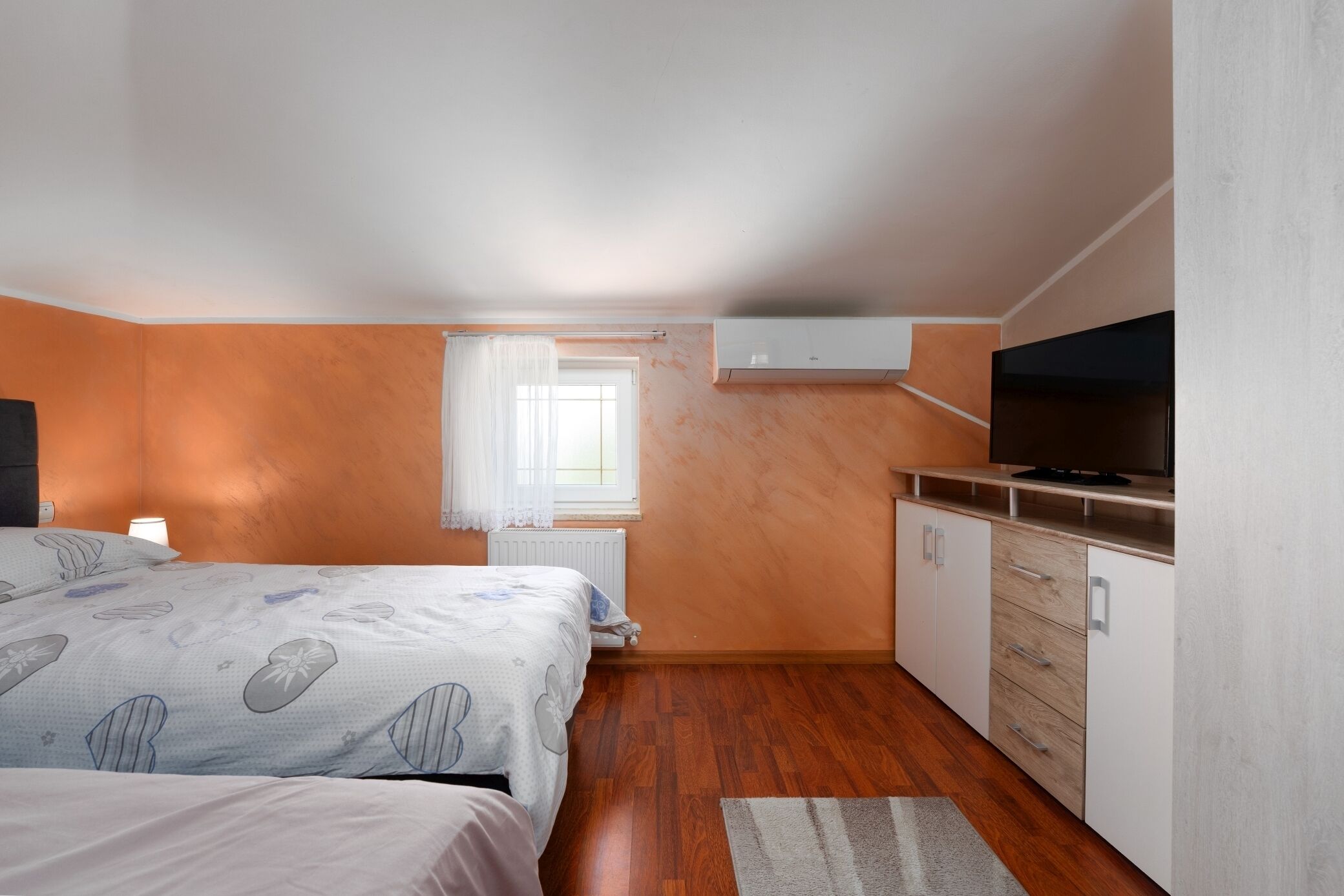 Une chambre avec deux lits, une télévision, une fenêtre avec des rideaux et un coin cuisine.