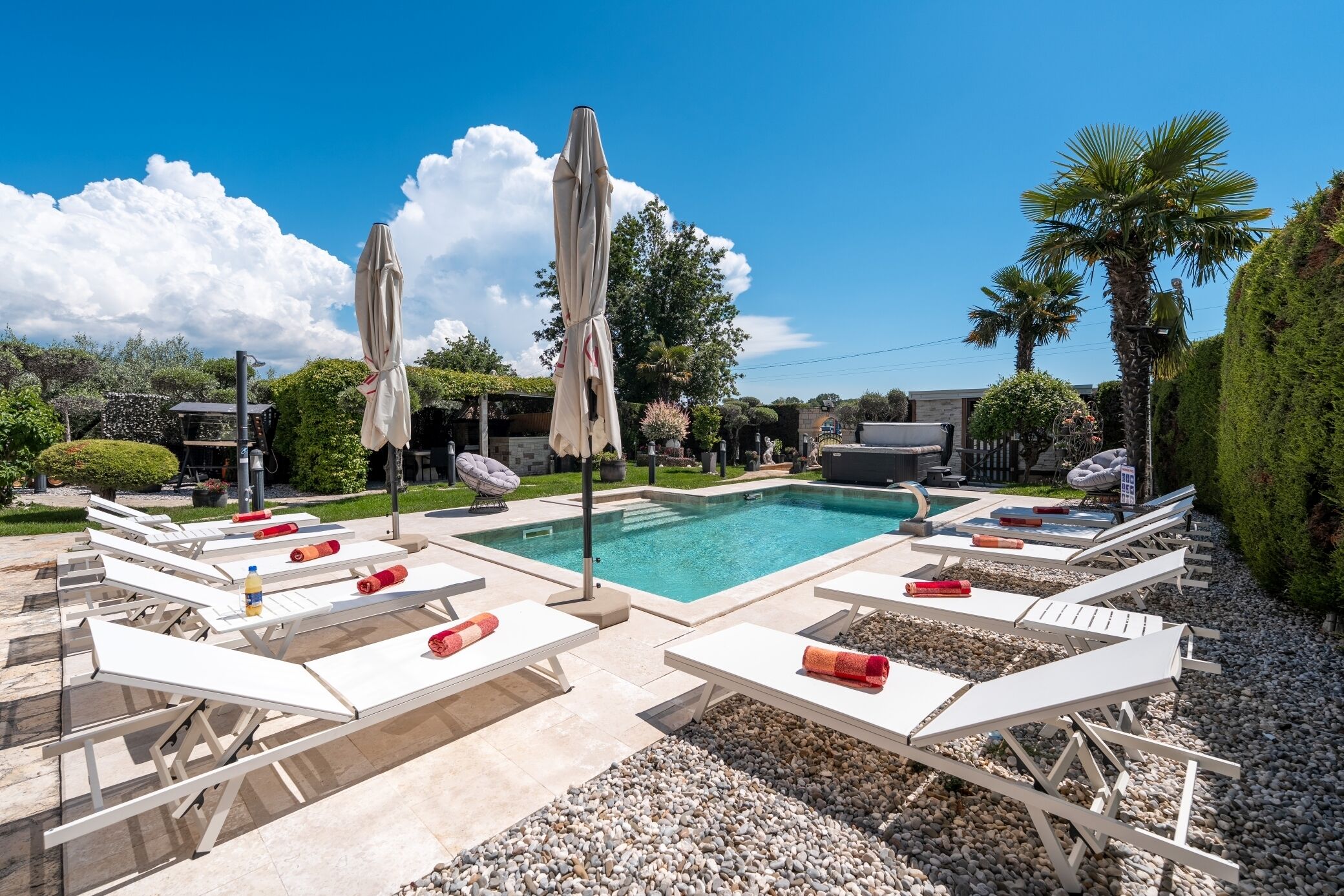 Un espace aménagé au bord de la piscine, avec des chaises longues et des parasols, une piscine et une végétation luxuriante tout autour.