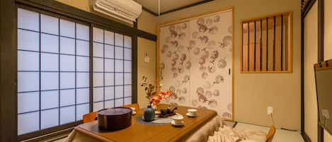 A traditional Japanese room with tatami flooring, a low table with a vase of flowers, and sliding doors with floral patterns.