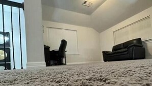 A carpeted room with a white ceiling, a black chair, and a black sofa.