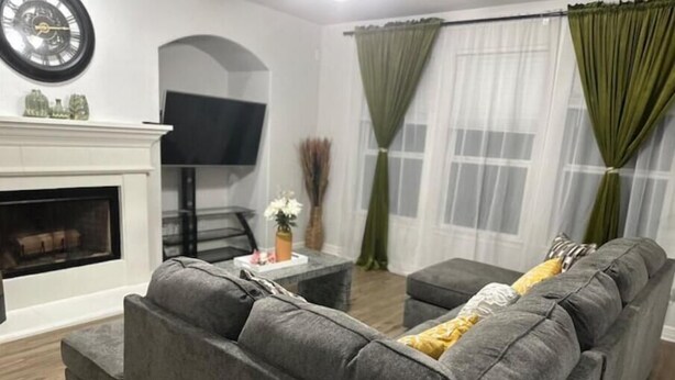 A living room with a gray sofa, a flat-screen TV, a fireplace, and green curtains.