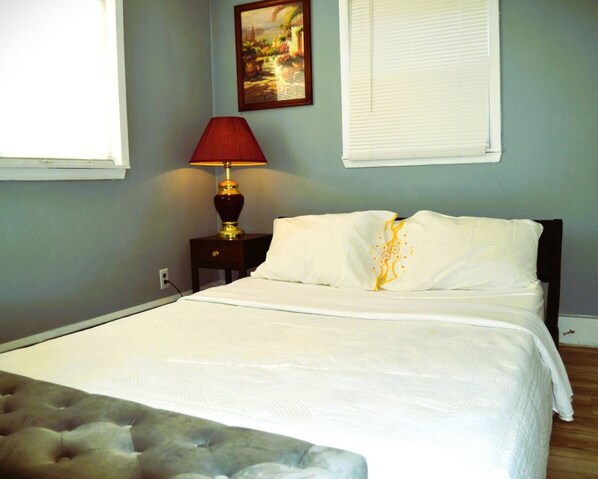 A neatly made bed with white linens, a red lamp on a bedside table, and a painting on the wall.