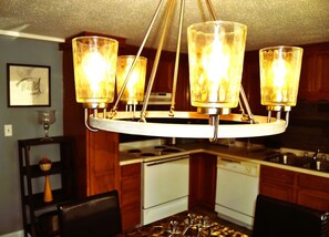 A chandelier with four glass shades and a wooden base, hanging in a kitchen with wooden cabinets and a white stove.