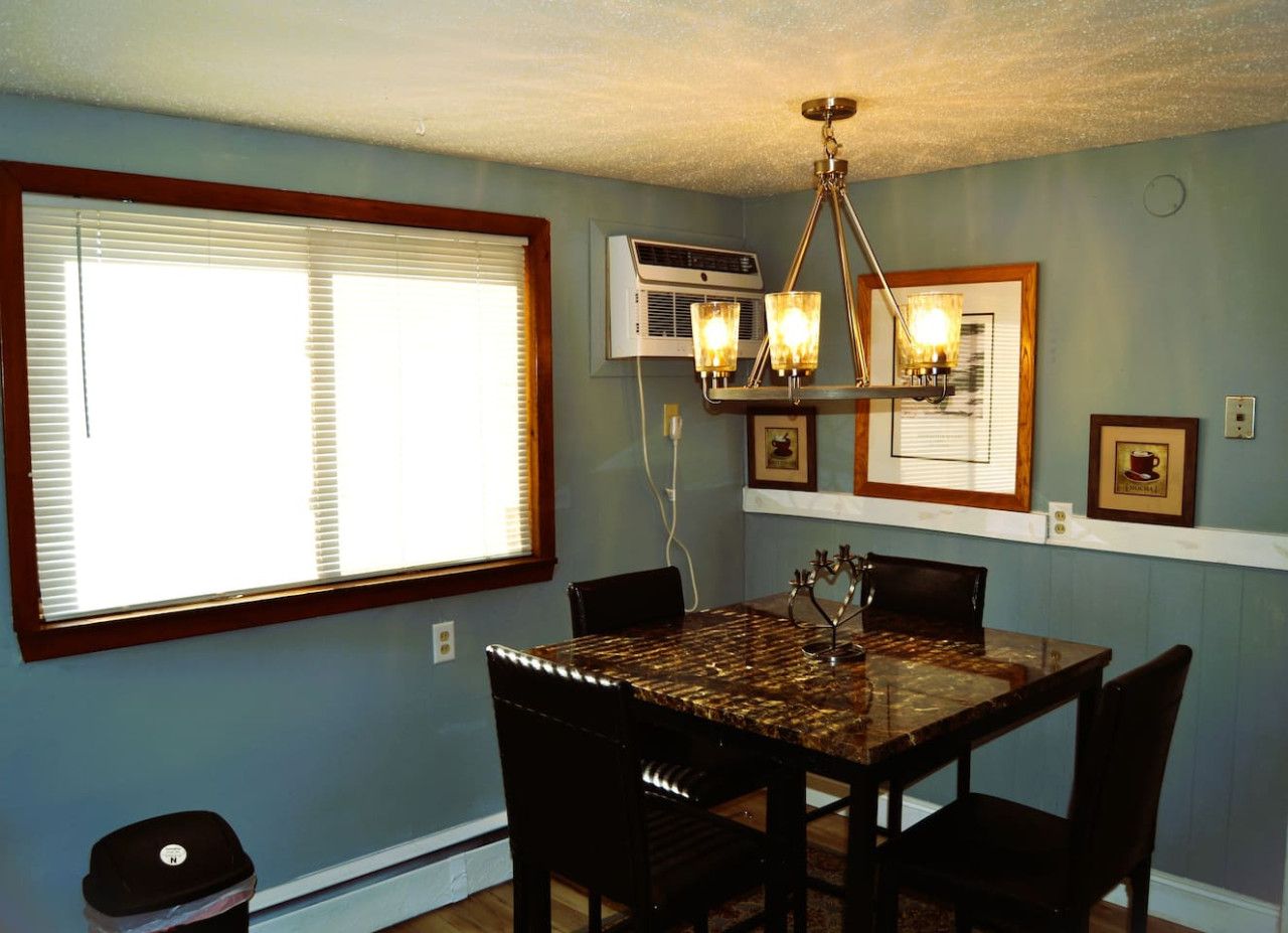 A dining area with a table, chairs, a chandelier, and wall-mounted air conditioning.