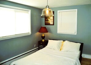 A bedroom with a bed, a nightstand, a lamp, and a picture on the wall.
