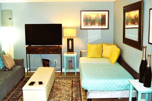 A hotel room with a bed, a sofa, a TV, a small table, and a lamp.
