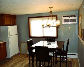 A kitchen with a dining table, chairs, a chandelier, a refrigerator, and an air conditioning unit.