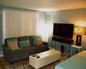 Una sala de estar con sofá, televisión, lámpara y alfombra estampada.