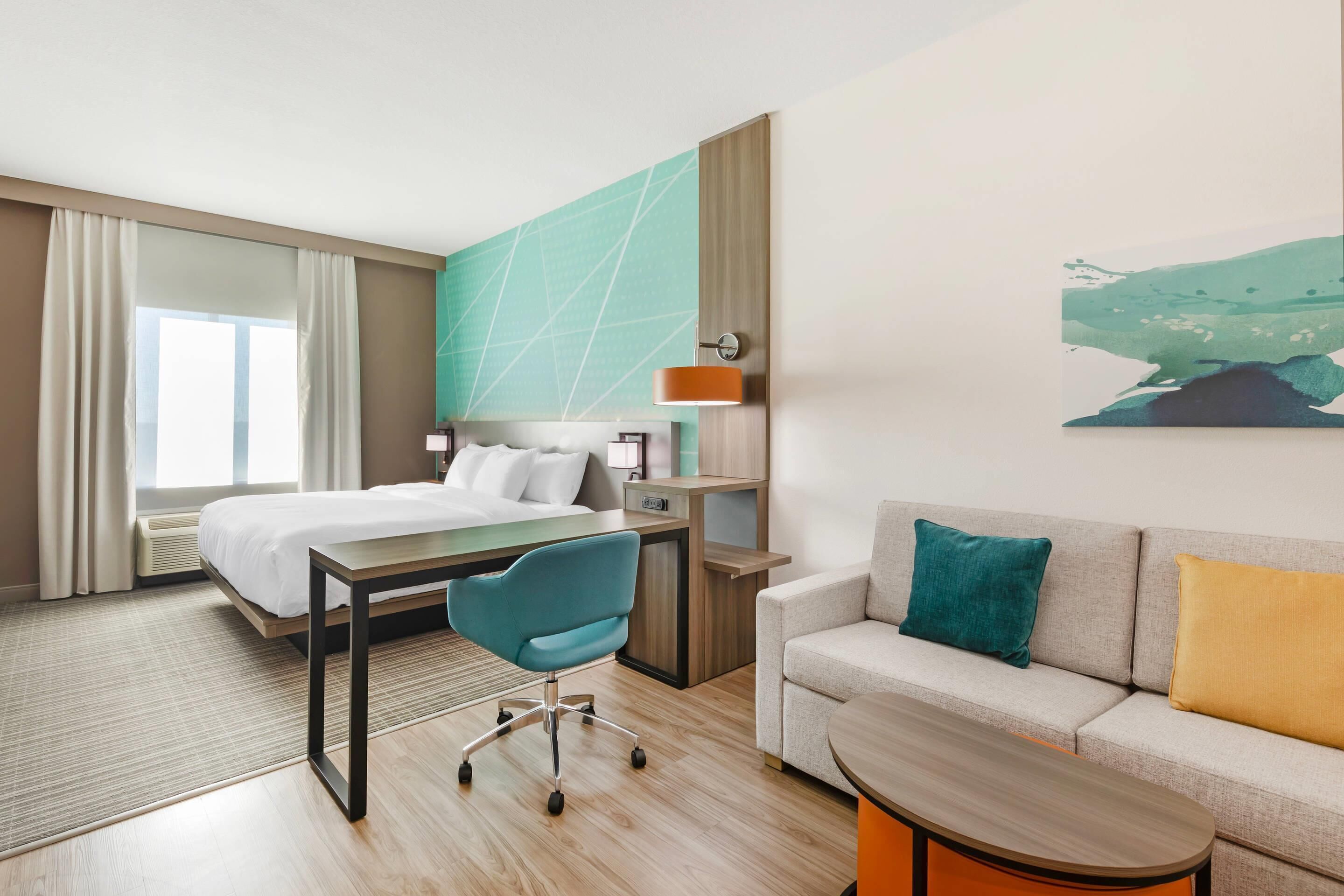 Habitación de hotel con cama, escritorio, silla, sofá y un cuadro en la pared.