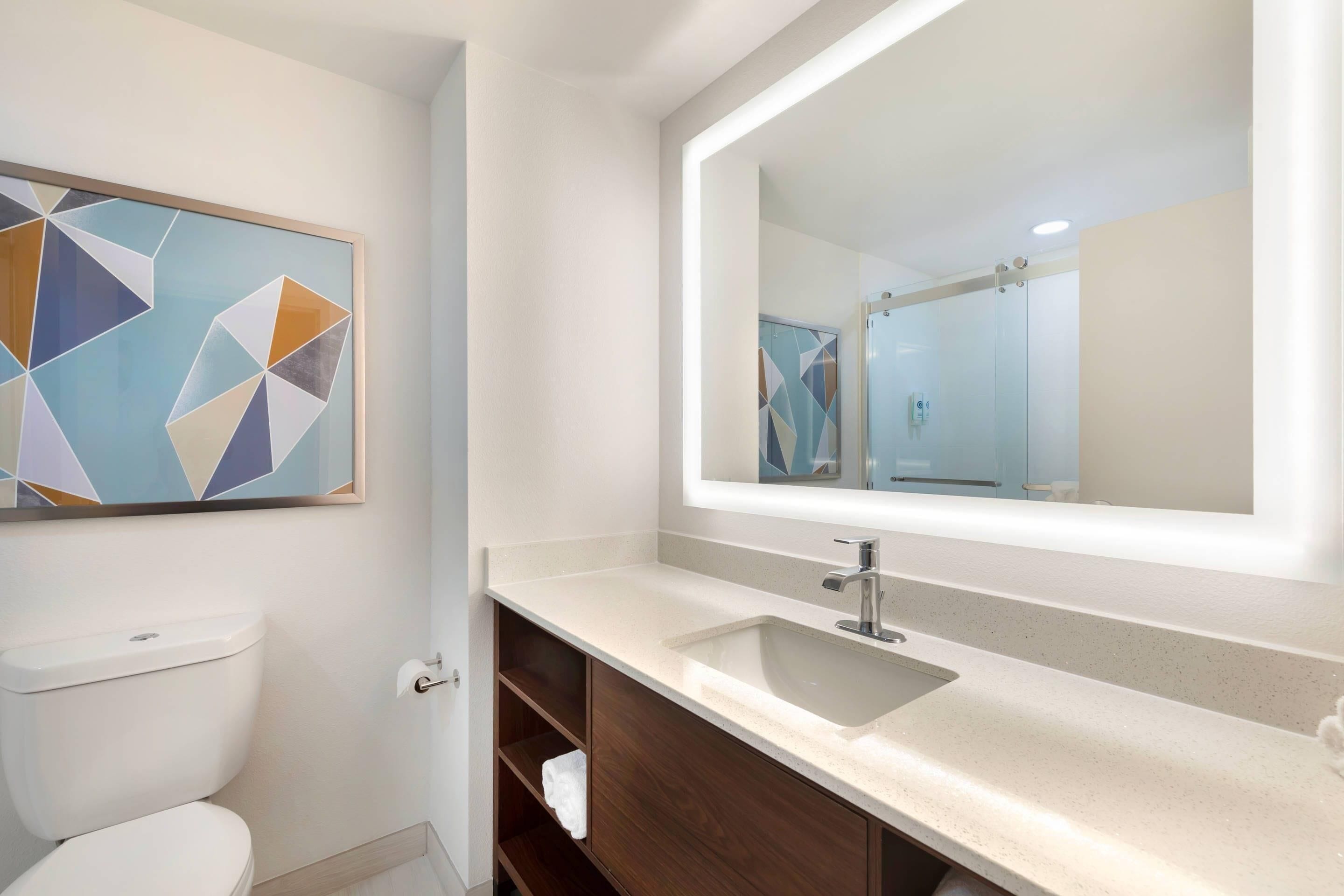 A modern bathroom with a toilet, a sink with a mirror, and a geometric artwork on the wall.
