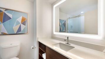 A modern bathroom with a toilet, a sink with a mirror, and a geometric artwork on the wall.