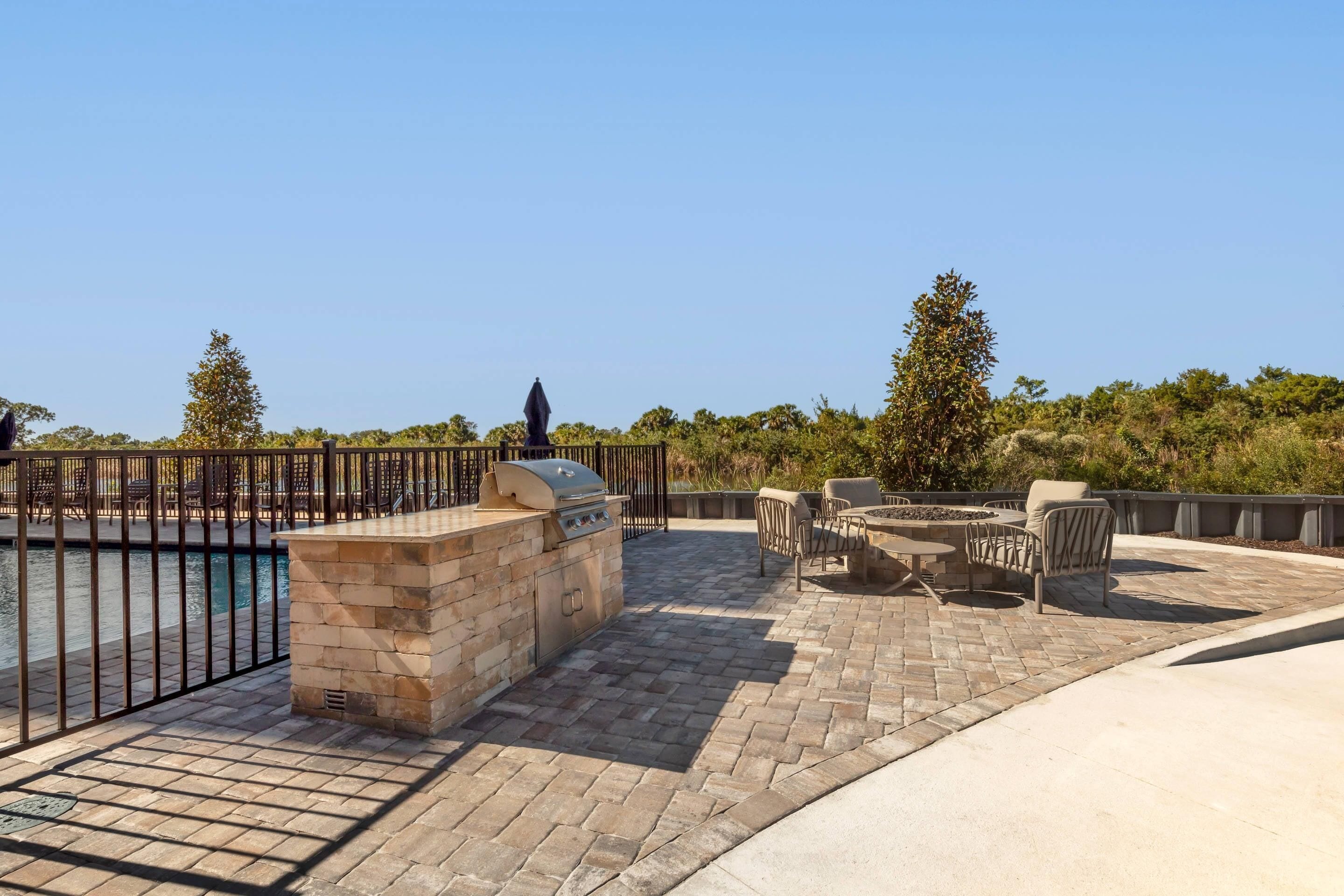 Un patio al aire libre con piscina, una barbacoa de piedra y mobiliario exterior.