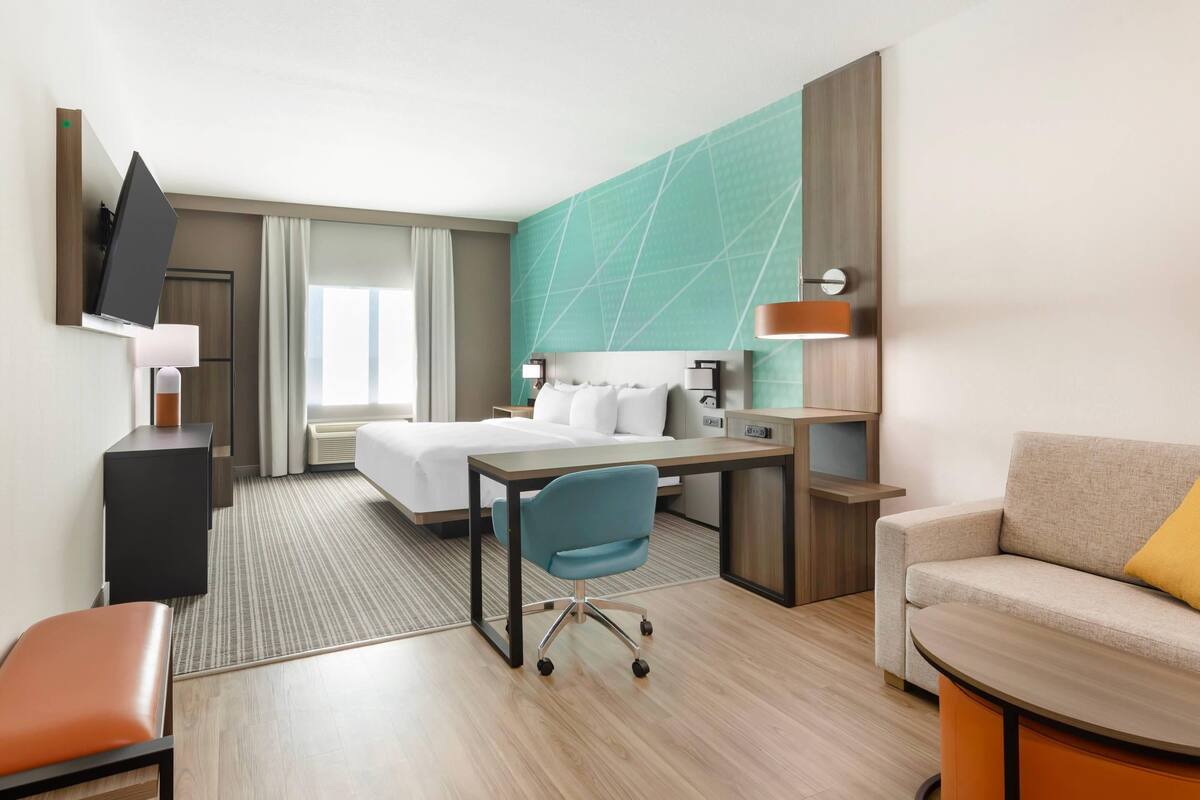 A hotel room with a bed, desk, chair, TV, and a sofa.