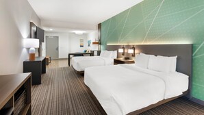 A hotel room with two beds, a desk, a chair, a TV, and a green accent wall.