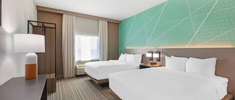 A hotel room with two beds, a desk, a lamp, and a large window with curtains.