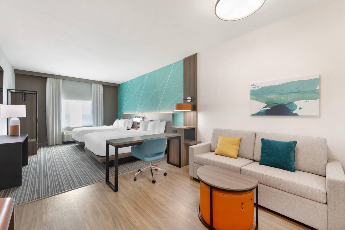 A hotel room with a bed, desk, sofa, and a painting on the wall.