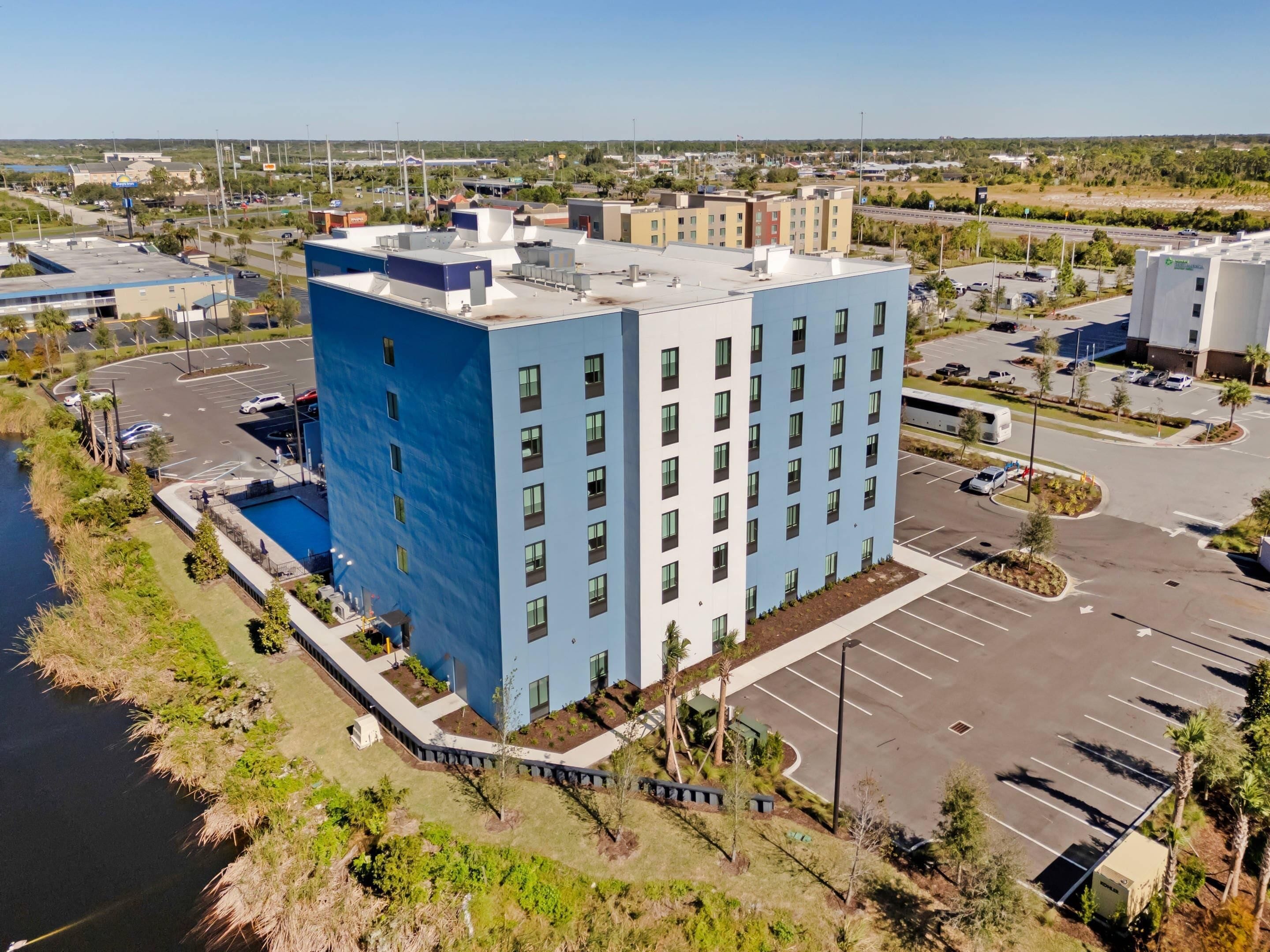 A multi-story hotel with a modern design, a parking lot, and a river adjacent to the building.