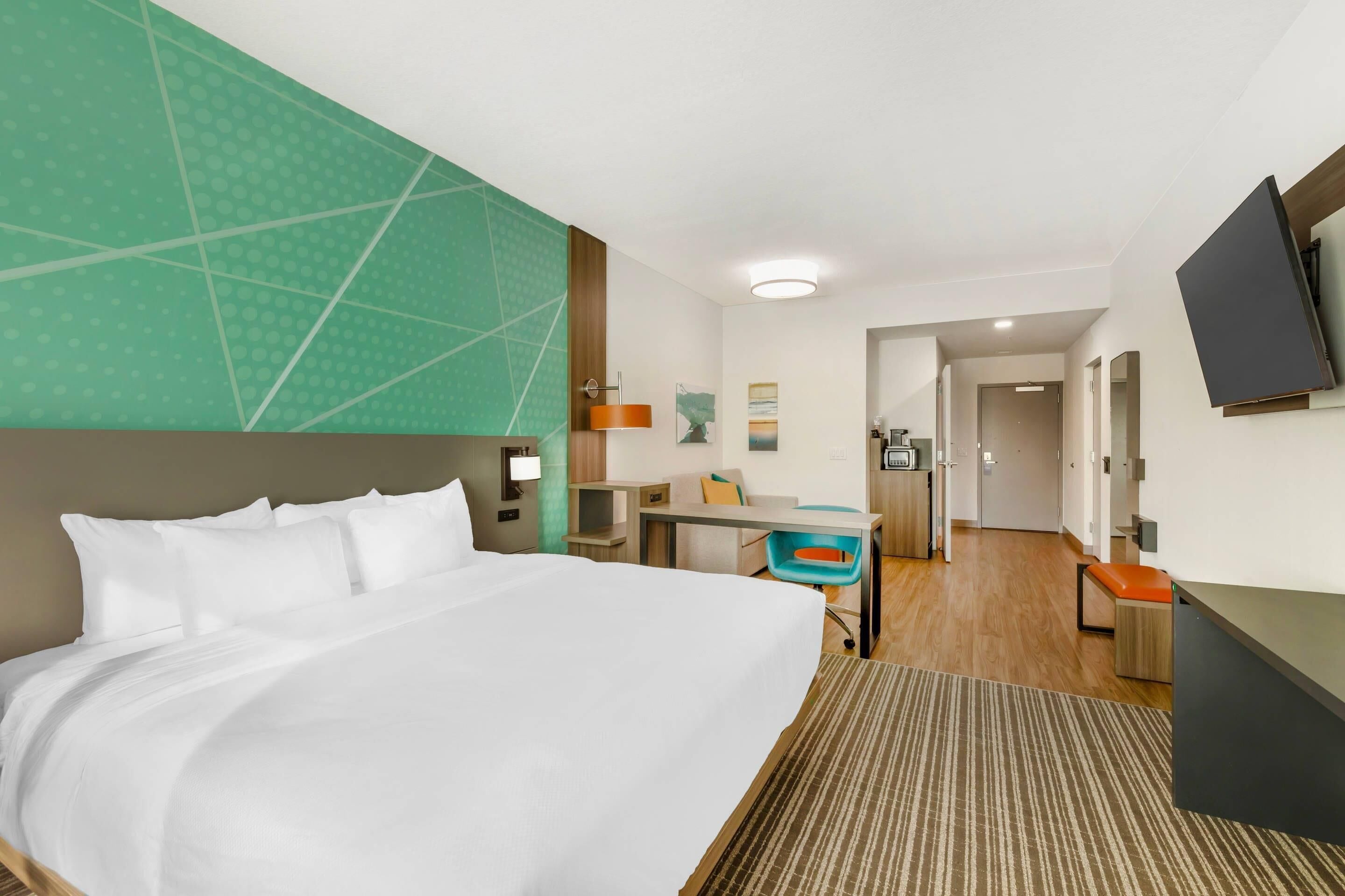 A hotel room with a large bed, a desk, a chair, a television, and a bathroom visible through an open door.