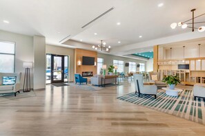 A spacious lobby with a wooden floor, modern furniture, a flat-screen TV, and a large window.