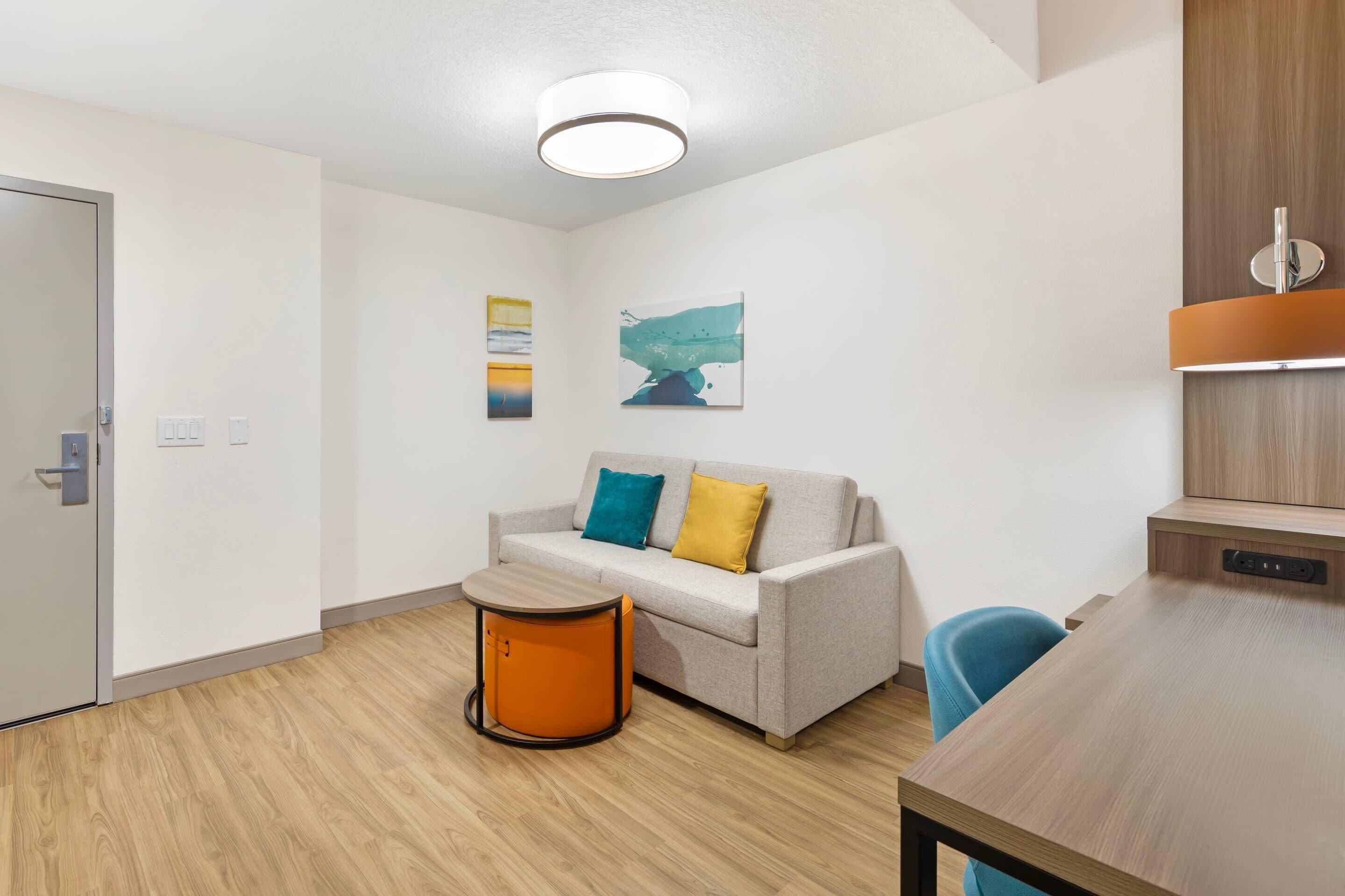 Une pièce moderne avec un canapé, une petite table ronde, un plancher en bois et un luminaire au plafond.