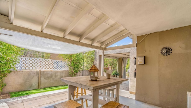 A covered patio with a wooden table and benches, a lantern, and a decorative wall piece. - Southwest‑Inspired Summer Place | Near UofA (Tucson)