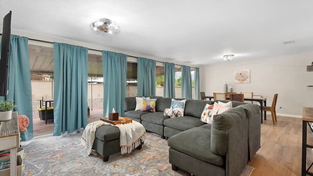 A living room with a sectional sofa, a coffee table, and a TV. There is a dining area with a table and chairs. - Eastside Family Summer Retreat | Yard & Games (Tucson)