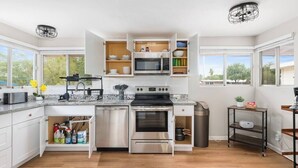 A modern kitchen with white cabinets, a stainless steel stove, a microwave, and a dishwasher. - Eastside Family Summer Retreat | Yard & Games (Tucson)