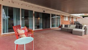 A covered patio area with a red chair, a grey sofa, and a small table. - Eastside Family Summer Retreat | Yard & Games (Tucson)