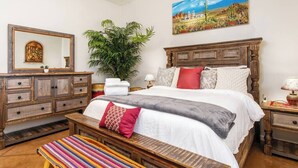 A bedroom with a wooden bed, a bench, a dresser, a mirror, and a large plant. - Cozy Summer Oasis | Near UofA & Shows (Tucson)