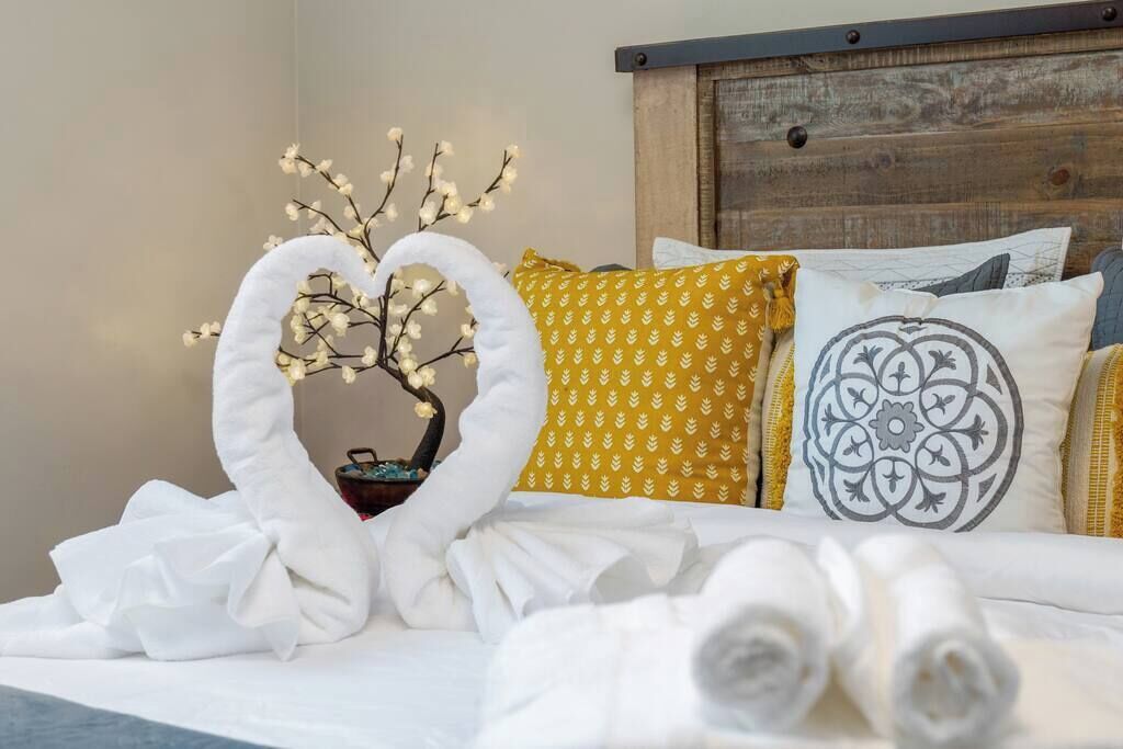 Una cama bien hecha con toallas enrolladas, una rama decorativa con luces y almohadas estampadas.
