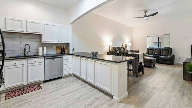 Una cocina moderna con armarios blancos, encimera negra y una zona de comedor con mesa y sillas de madera oscura.
