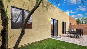 Una casa con un patio, un comedor con sillas y una puerta que da al interior.