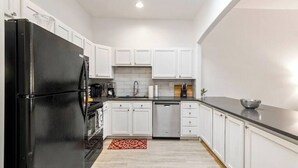 Una cocina moderna con armarios blancos, un refrigerador negro, un lavavajillas y una encimera negra.
