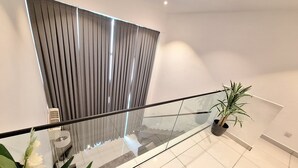 A modern interior with a glass railing, a potted plant, and a large window with vertical blinds. - The Gem of Embassy Gardens  (Accra)